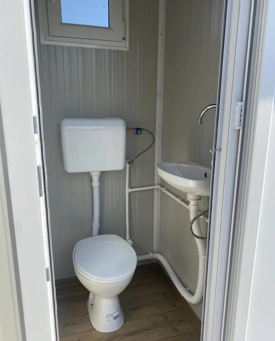 Flushing restroom cabin interior with tank toilet and wall sink