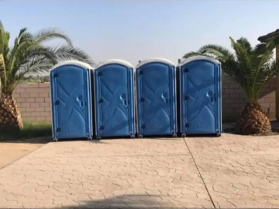 Row of four blue porta potties on a paved lot