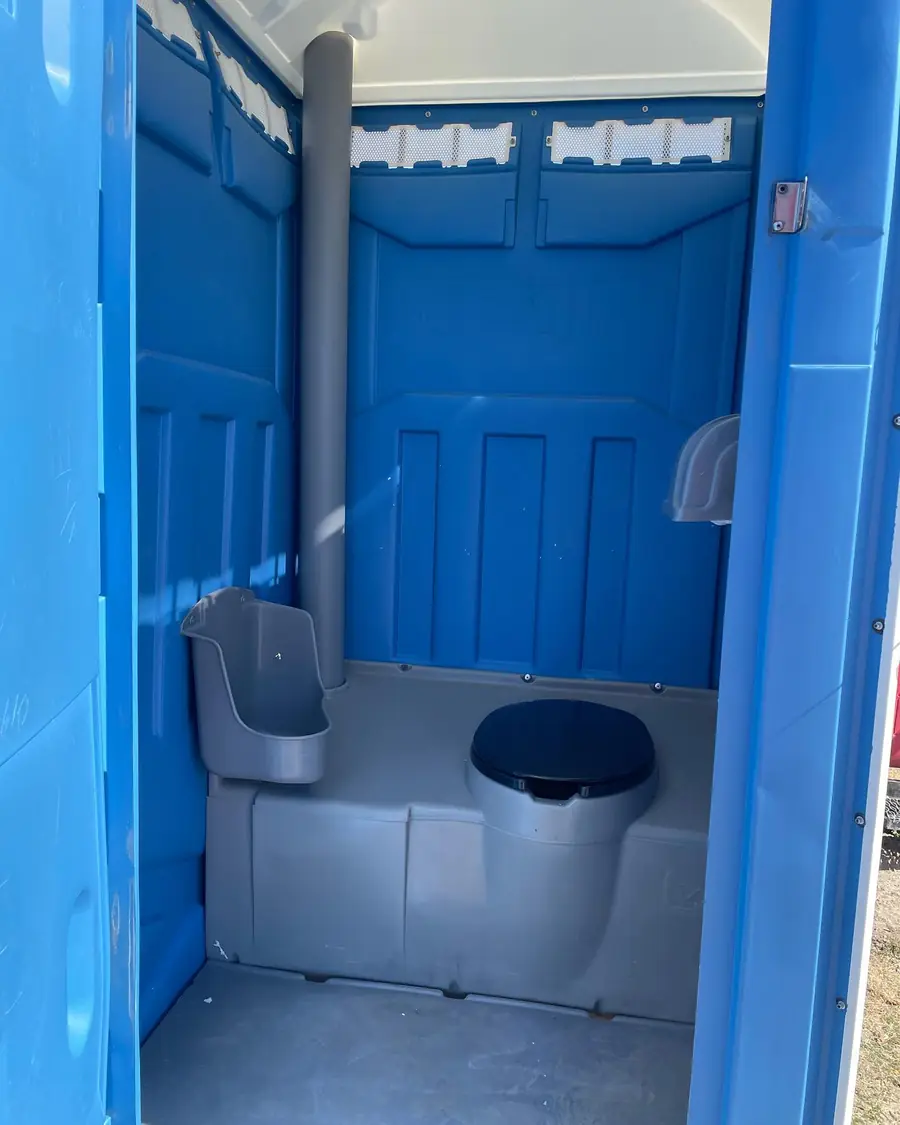 Clean interior of a blue standard porta potty with seat, urinal and vent pipe
