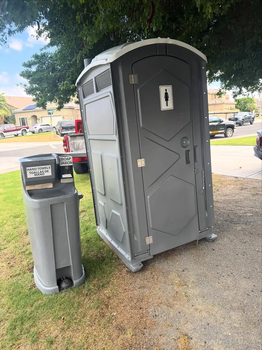 Gray portable toilet next to a freestanding handwashing station on a lawn